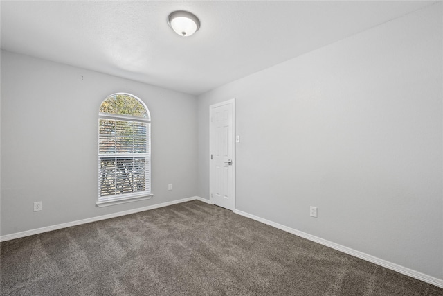 spare room with dark colored carpet and baseboards