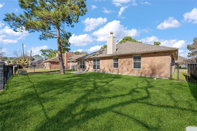 back of house featuring a fenced backyard, brick siding, a yard, roof with shingles, and a chimney