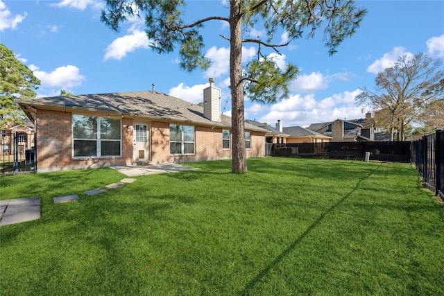 back of house with brick siding, a chimney, a fenced backyard, and a lawn