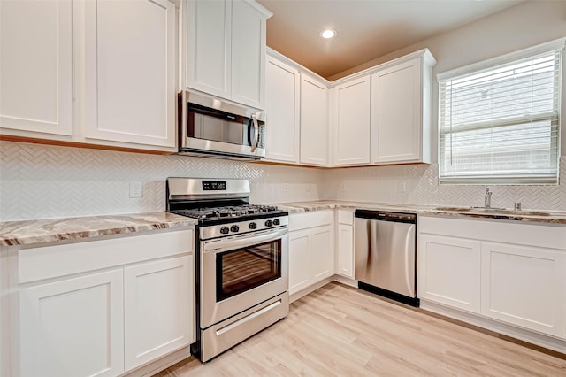 kitchen featuring sink, appliances with stainless steel finishes, light stone countertops, light hardwood / wood-style floors, and white cabinets