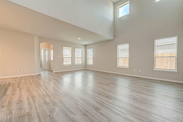 unfurnished living room featuring a towering ceiling, a wealth of natural light, and light hardwood / wood-style flooring