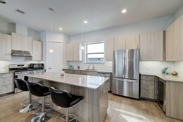 kitchen with a breakfast bar, sink, a center island, stainless steel appliances, and light hardwood / wood-style flooring