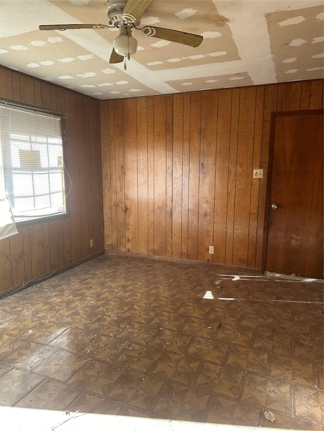 unfurnished room with ceiling fan and wood walls