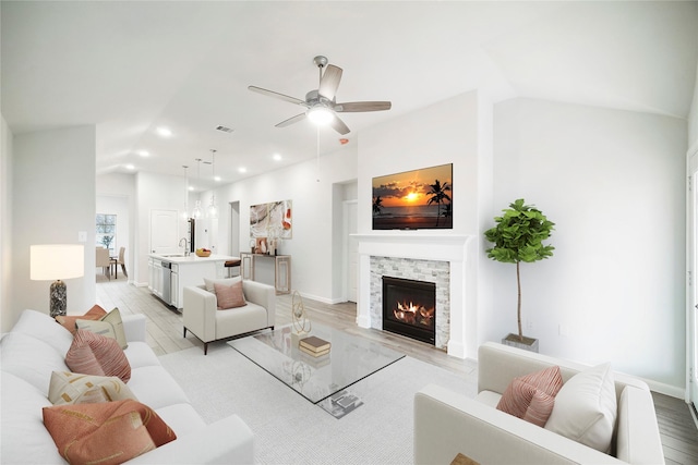 living room featuring sink, vaulted ceiling, a fireplace, and light wood-type flooring