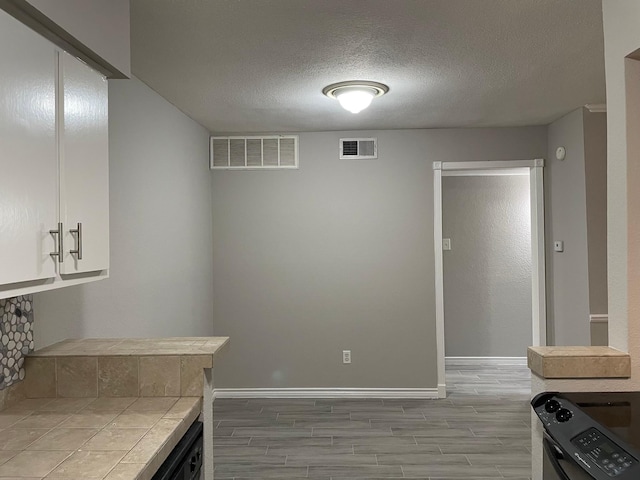 kitchen with white cabinetry, tile countertops, light hardwood / wood-style flooring, a textured ceiling, and black range with electric stovetop