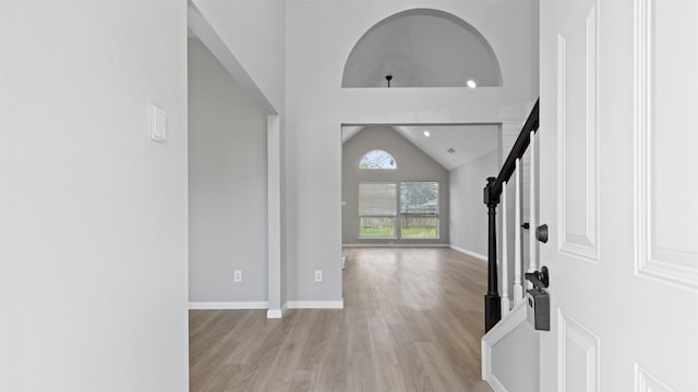 foyer with light wood-style floors, stairs, baseboards, and vaulted ceiling