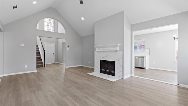 unfurnished living room featuring light wood-style flooring, stairway, a premium fireplace, high vaulted ceiling, and baseboards