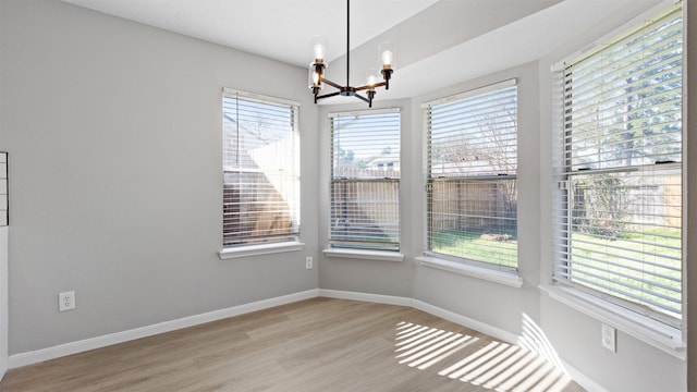 unfurnished dining area with a chandelier, light wood-type flooring, and baseboards