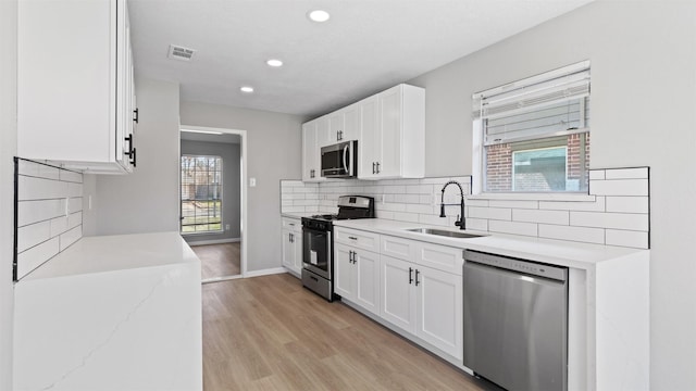 kitchen with stainless steel appliances, backsplash, white cabinets, a sink, and light wood-type flooring