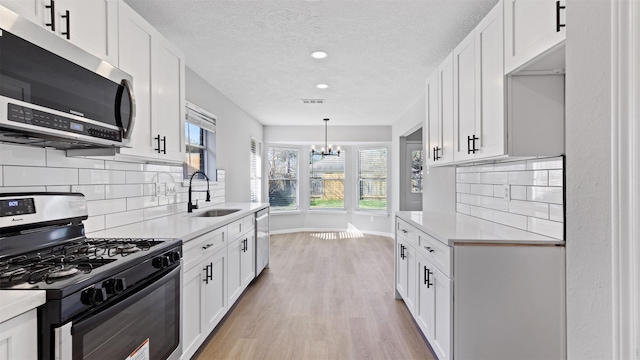 kitchen with light countertops, light wood-style flooring, appliances with stainless steel finishes, white cabinetry, and a sink