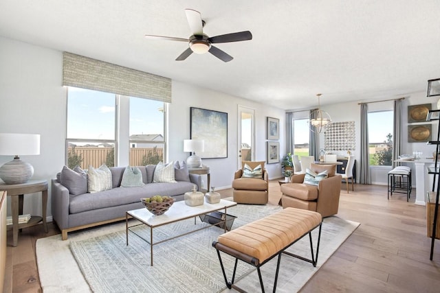 living room with ceiling fan with notable chandelier and light hardwood / wood-style flooring