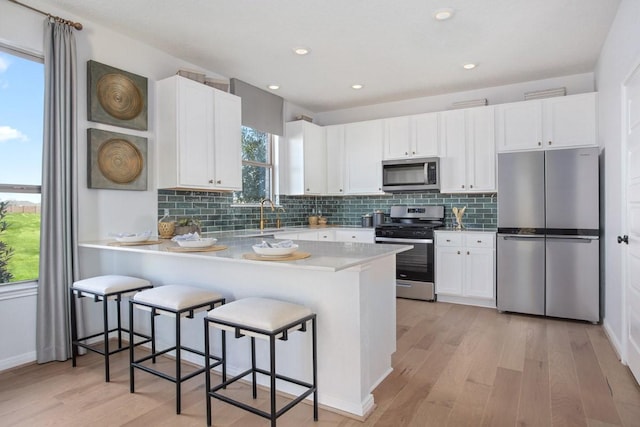 kitchen with stainless steel appliances, kitchen peninsula, a breakfast bar area, and white cabinets