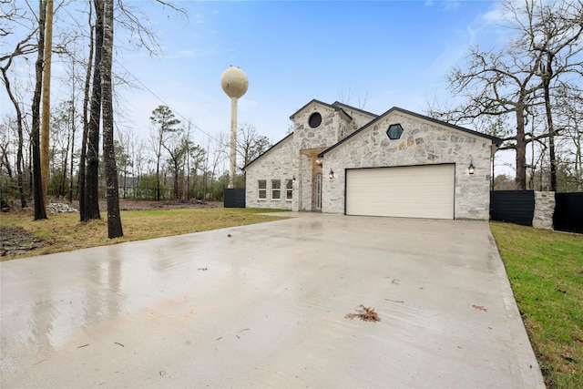 french country style house featuring concrete driveway, stone siding, an attached garage, fence, and a front lawn