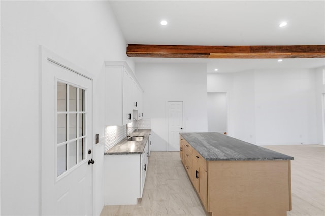 kitchen featuring sink, light hardwood / wood-style flooring, a kitchen island, light brown cabinetry, and beamed ceiling