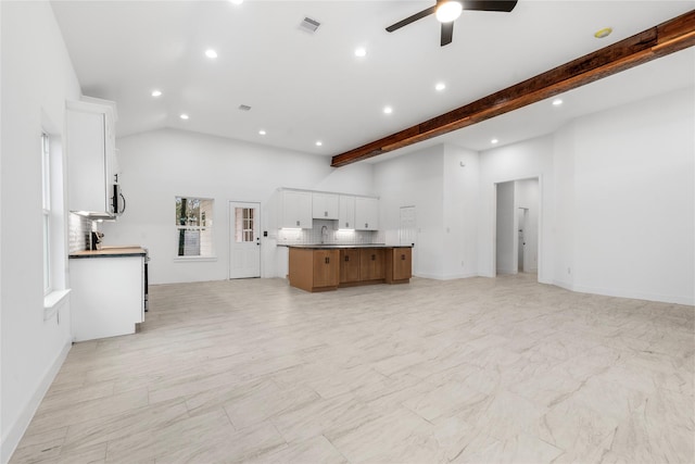 kitchen with tasteful backsplash, lofted ceiling with beams, white cabinets, a large island, and ceiling fan