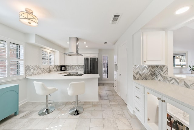 kitchen featuring a kitchen bar, black appliances, kitchen peninsula, island exhaust hood, and white cabinets