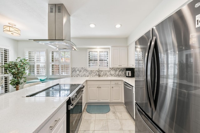 kitchen with appliances with stainless steel finishes, white cabinetry, sink, backsplash, and island exhaust hood