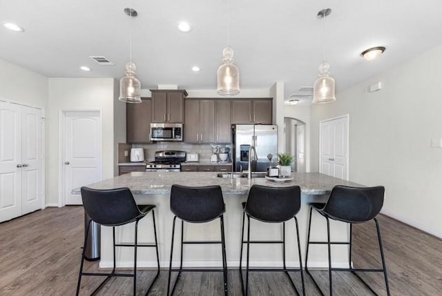 kitchen featuring stainless steel appliances, light stone countertops, a kitchen island with sink, and decorative light fixtures