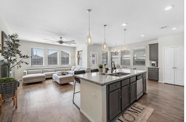 kitchen with sink, light stone counters, hanging light fixtures, stainless steel dishwasher, and a kitchen island with sink