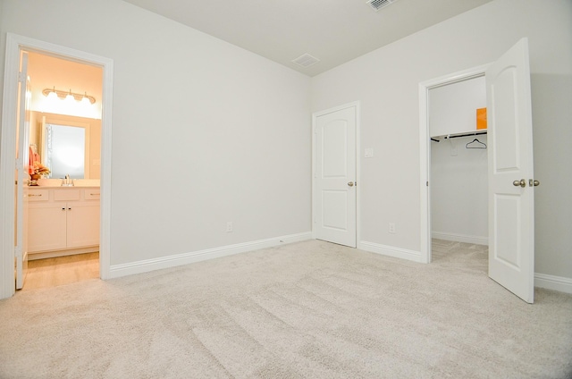 unfurnished bedroom with sink, ensuite bath, a spacious closet, a closet, and light colored carpet