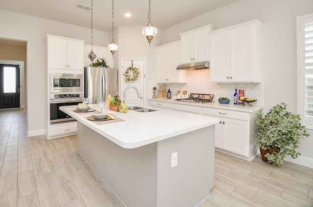 kitchen featuring sink, appliances with stainless steel finishes, white cabinetry, hanging light fixtures, and an island with sink