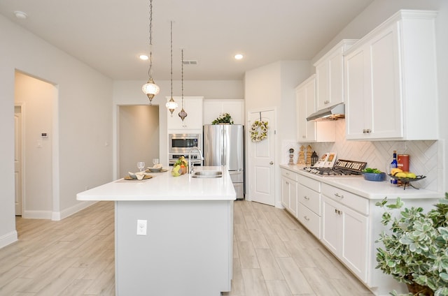 kitchen featuring appliances with stainless steel finishes, decorative backsplash, an island with sink, white cabinets, and decorative light fixtures