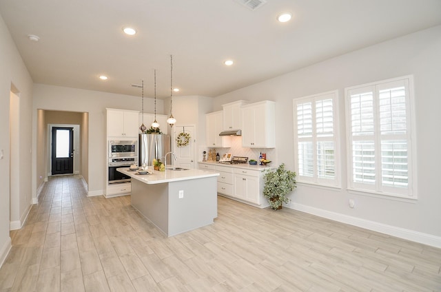 kitchen featuring tasteful backsplash, decorative light fixtures, a center island with sink, appliances with stainless steel finishes, and white cabinets