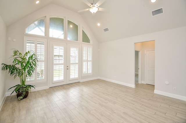 empty room with ceiling fan, high vaulted ceiling, a healthy amount of sunlight, and light wood-type flooring