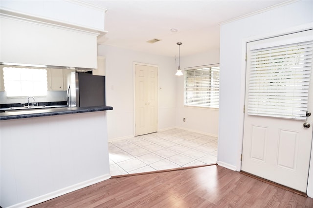 kitchen featuring sink, stainless steel fridge, light hardwood / wood-style flooring, white cabinetry, and hanging light fixtures