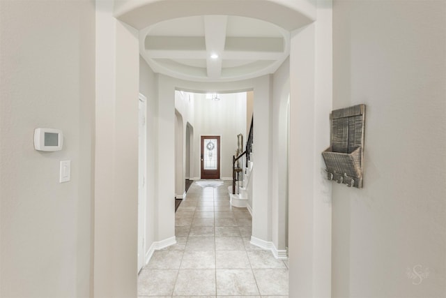 hall featuring a towering ceiling, coffered ceiling, beam ceiling, and light tile patterned floors