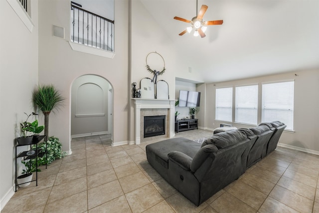 living room featuring a tiled fireplace, ceiling fan, light tile patterned floors, and high vaulted ceiling