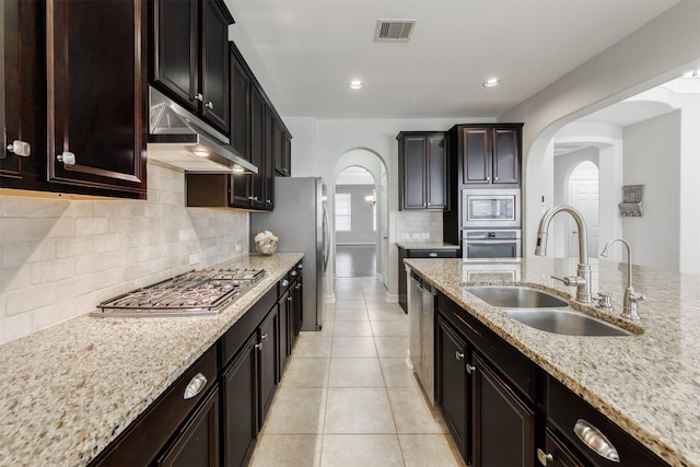 kitchen featuring sink, light tile patterned floors, backsplash, stainless steel appliances, and light stone counters