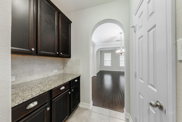 kitchen featuring tasteful backsplash, ornamental molding, light tile patterned floors, dark brown cabinetry, and light stone counters