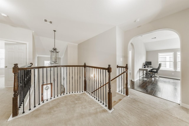 corridor featuring light carpet, lofted ceiling, and an inviting chandelier