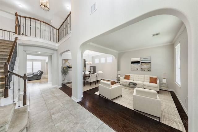 living room with an inviting chandelier, ornamental molding, light hardwood / wood-style flooring, and a high ceiling