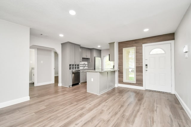 kitchen featuring light stone counters, gray cabinets, dishwasher, and light wood-type flooring