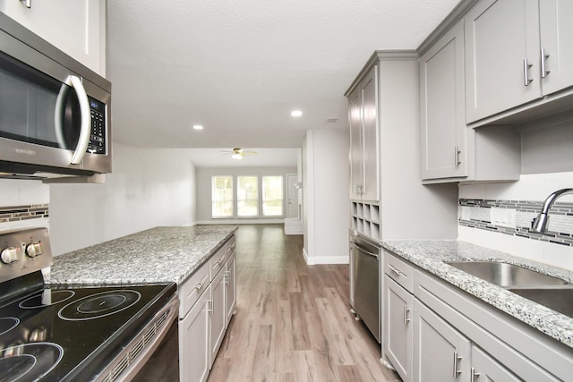 kitchen with sink, backsplash, ceiling fan, light hardwood / wood-style floors, and stainless steel appliances