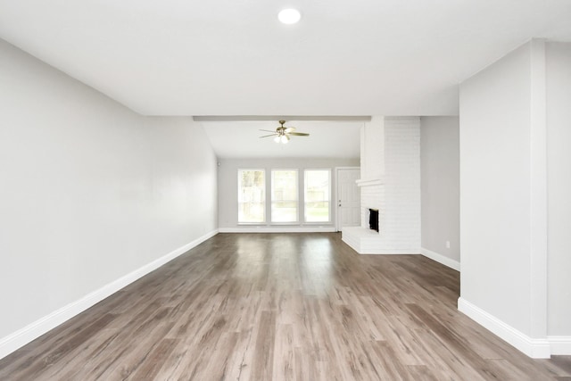 unfurnished living room with wood-type flooring, a brick fireplace, and ceiling fan