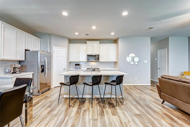 kitchen featuring white cabinetry, stainless steel appliances, light hardwood / wood-style floors, and a center island with sink