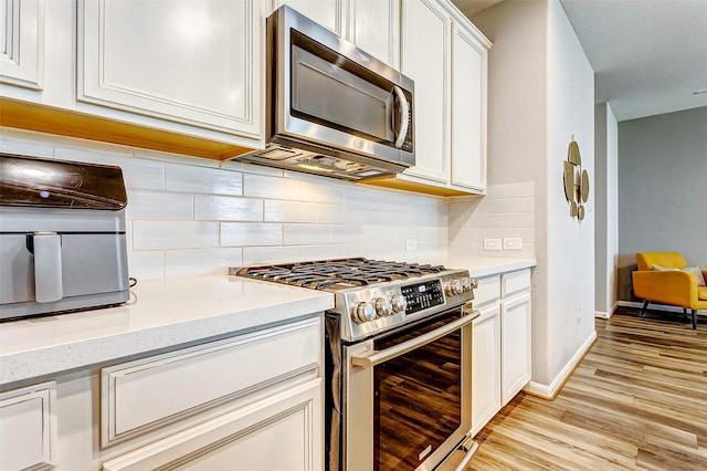 kitchen with appliances with stainless steel finishes, white cabinets, decorative backsplash, light stone countertops, and light hardwood / wood-style flooring