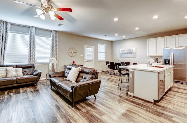 living room featuring ceiling fan, sink, and light wood-type flooring