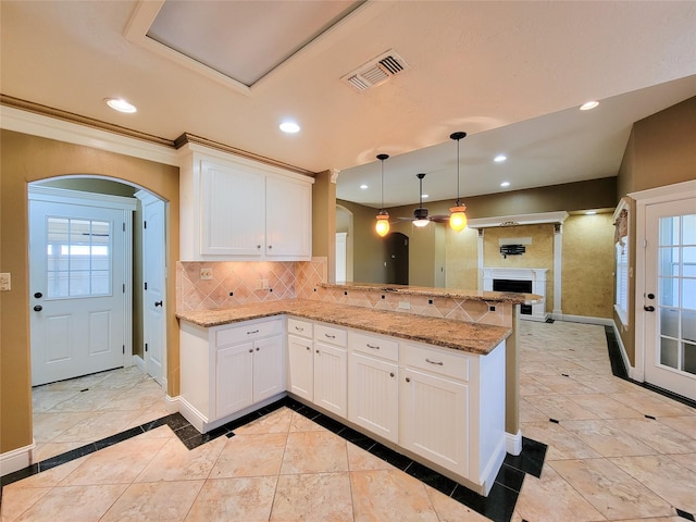 kitchen with light stone counters, decorative backsplash, kitchen peninsula, and white cabinets