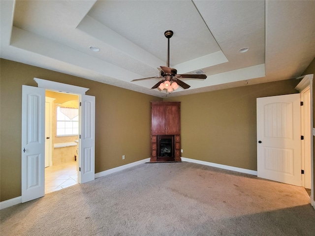 unfurnished living room with a raised ceiling, light colored carpet, and ceiling fan