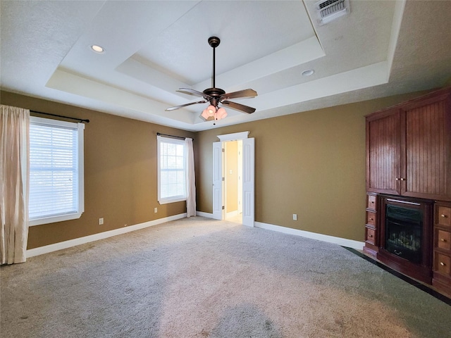 unfurnished living room with light colored carpet, a raised ceiling, and ceiling fan