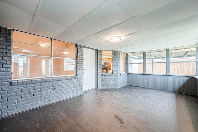 empty room with brick wall, hardwood / wood-style floors, and a paneled ceiling