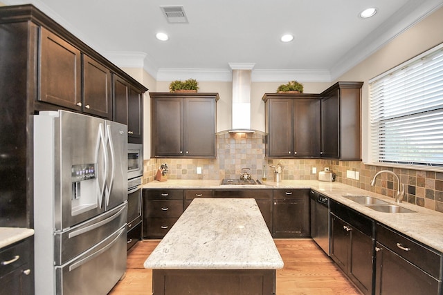 kitchen featuring appliances with stainless steel finishes, wall chimney range hood, a center island, sink, and light wood-type flooring