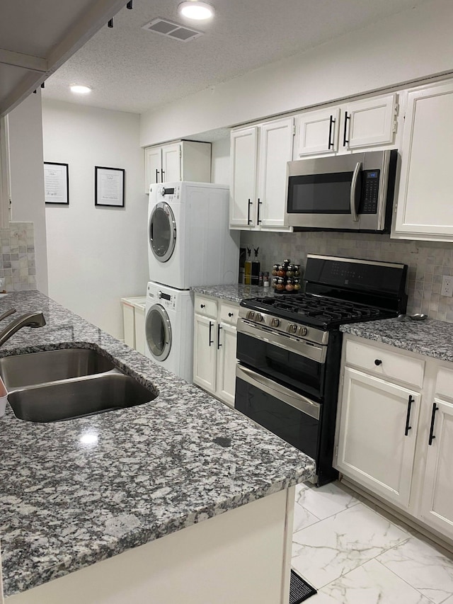 kitchen with sink, white cabinetry, double oven range, stacked washer / dryer, and stone countertops