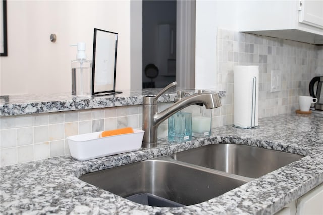 interior details featuring tasteful backsplash, sink, white cabinets, and light stone counters