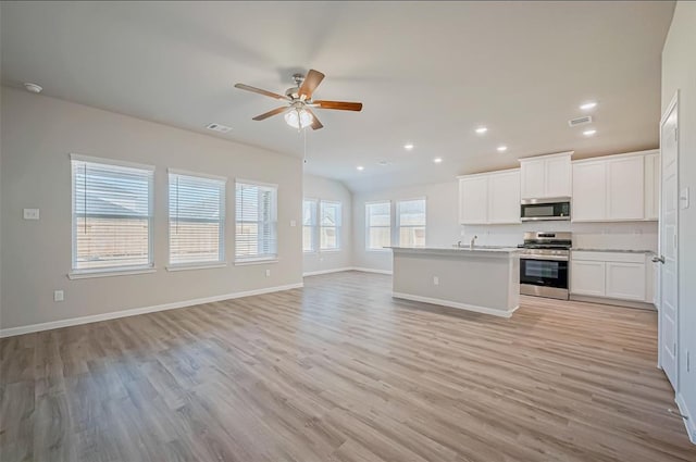 kitchen with ceiling fan, appliances with stainless steel finishes, light hardwood / wood-style floors, an island with sink, and white cabinets