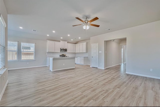 kitchen with light hardwood / wood-style flooring, an island with sink, ceiling fan, stainless steel appliances, and white cabinets